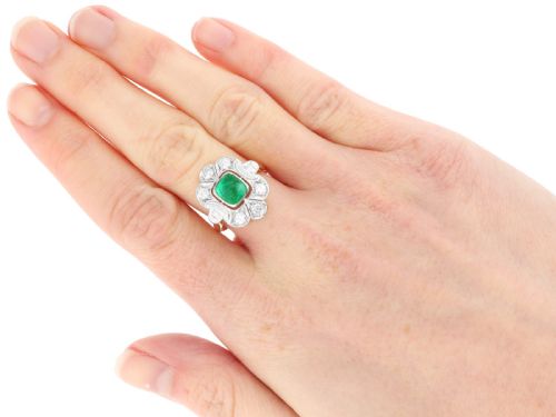 fig 8. An Art Deco dress ring featuring a central cushion-cut green emerald surrounded by a geometric pierced diamond halo set in white metal on an 18ct yellow gold band.