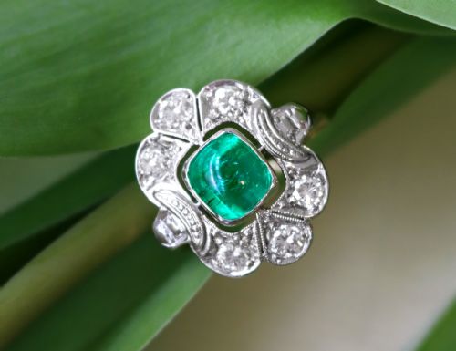 fig 3. An Art Deco dress ring featuring a central cushion-cut green emerald surrounded by a geometric pierced diamond halo set in white metal on an 18ct yellow gold band.
