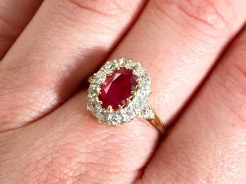 fig 2. An 18ct yellow gold ring featuring a central oval faceted ruby surrounded by a halo of twelve old cut diamonds in claw settings.