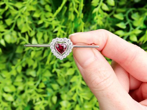 fig 1. A vintage 18k white gold bar brooch featuring a central heart-cut red ruby framed by a diamond halo, mounted on a slender polished bar.