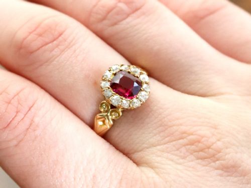 fig 2. An 18ct yellow gold Victorian cluster ring featuring a central cushion-cut red ruby framed by twelve hand-cut diamonds with carved scroll shoulders.