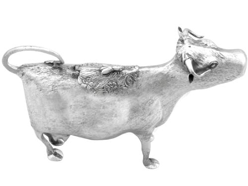 fig 2. An antique sterling silver cow creamer featuring textured hide detailing, a looped tail handle, and a floral hinged lid on its back.