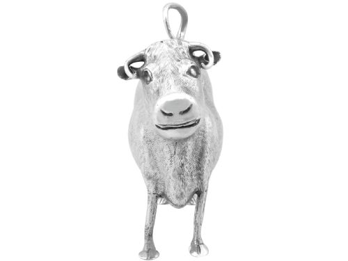 fig 4. An antique sterling silver cow creamer featuring textured hide detailing, a looped tail handle, and a floral hinged lid on its back.