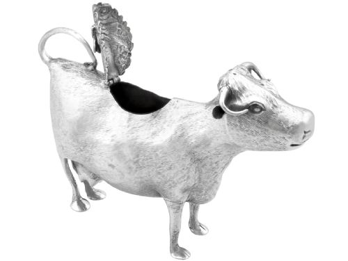 fig 7. An antique sterling silver cow creamer featuring textured hide detailing, a looped tail handle, and a floral hinged lid on its back.
