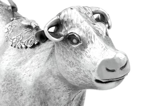 fig 8. An antique sterling silver cow creamer featuring textured hide detailing, a looped tail handle, and a floral hinged lid on its back.