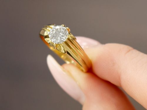 fig 2. An 18ct yellow gold solitaire ring featuring a round central diamond held in a claw setting with fluted shoulders.
