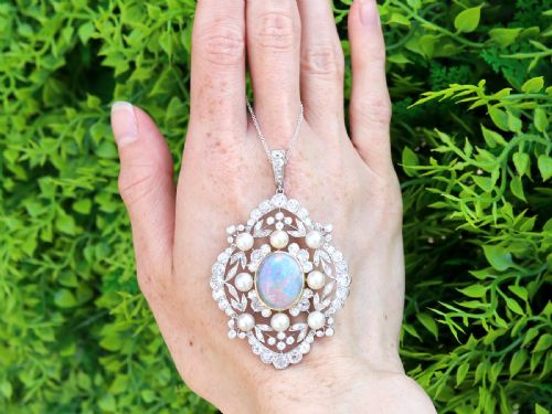 fig 1. An antique platinum pendant featuring a central oval cabochon opal set in gold, surrounded by natural saltwater pearls and openwork diamond filigree.