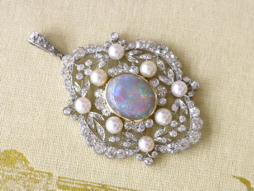fig 2. An antique platinum pendant featuring a central oval cabochon opal set in gold, surrounded by natural saltwater pearls and openwork diamond filigree.