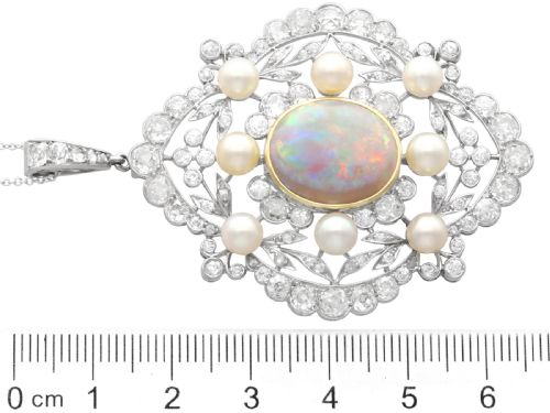 fig 6. An antique platinum pendant featuring a central oval cabochon opal set in gold, surrounded by natural saltwater pearls and openwork diamond filigree.
