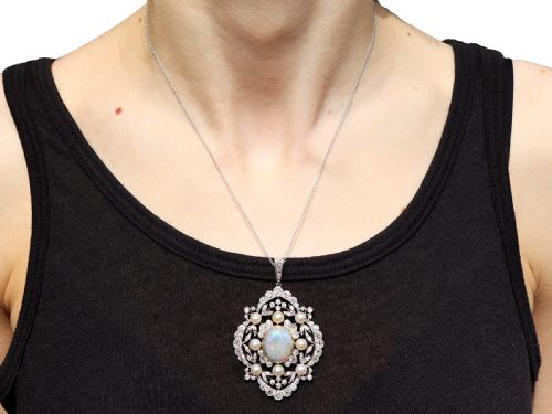 fig 7. An antique platinum pendant featuring a central oval cabochon opal set in gold, surrounded by natural saltwater pearls and openwork diamond filigree.