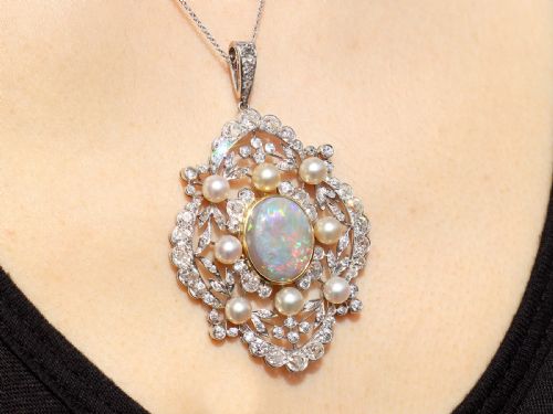 fig 8. An antique platinum pendant featuring a central oval cabochon opal set in gold, surrounded by natural saltwater pearls and openwork diamond filigree.