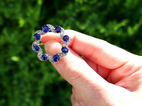 fig 1. A circular late Victorian wreath brooch set with eight oval blue sapphires and diamond-set silver ribbon scroll motifs on a yellow gold frame.