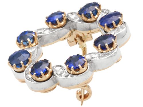 fig 3. A circular late Victorian wreath brooch set with eight oval blue sapphires and diamond-set silver ribbon scroll motifs on a yellow gold frame.