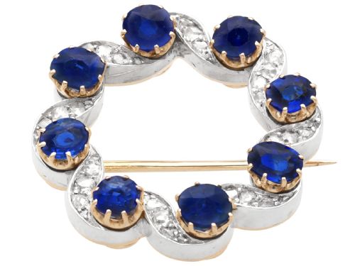 fig 4. A circular late Victorian wreath brooch set with eight oval blue sapphires and diamond-set silver ribbon scroll motifs on a yellow gold frame.