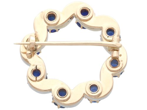 fig 5. A circular late Victorian wreath brooch set with eight oval blue sapphires and diamond-set silver ribbon scroll motifs on a yellow gold frame.