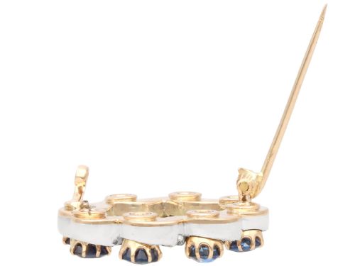 fig 6. A circular late Victorian wreath brooch set with eight oval blue sapphires and diamond-set silver ribbon scroll motifs on a yellow gold frame.