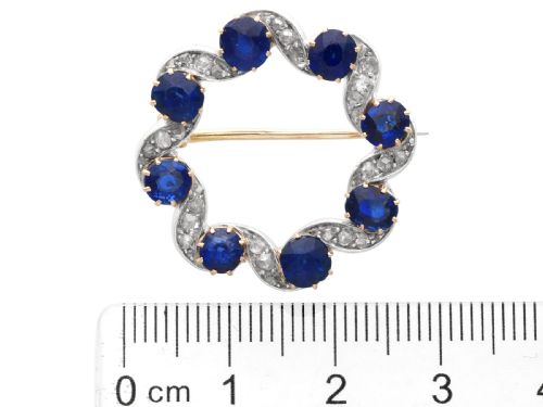 fig 7. A circular late Victorian wreath brooch set with eight oval blue sapphires and diamond-set silver ribbon scroll motifs on a yellow gold frame.