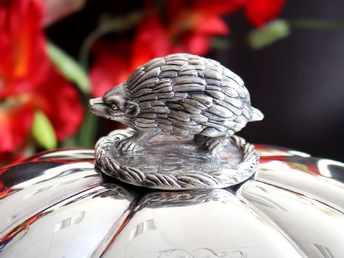 fig 1. An antique silver soup tureen featuring a lobed body, scrolled acanthus feet, double side handles, and a domed lid topped with an animal finial.