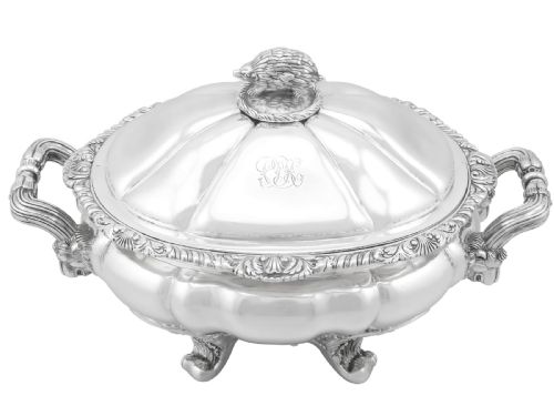fig 2. An antique silver soup tureen featuring a lobed body, scrolled acanthus feet, double side handles, and a domed lid topped with an animal finial.