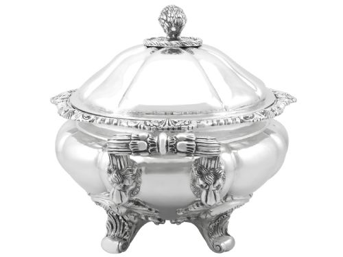 fig 4. An antique silver soup tureen featuring a lobed body, scrolled acanthus feet, double side handles, and a domed lid topped with an animal finial.