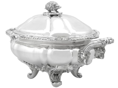 fig 5. An antique silver soup tureen featuring a lobed body, scrolled acanthus feet, double side handles, and a domed lid topped with an animal finial.