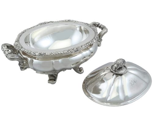 fig 6. An antique silver soup tureen featuring a lobed body, scrolled acanthus feet, double side handles, and a domed lid topped with an animal finial.