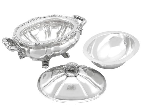 fig 7. An antique silver soup tureen featuring a lobed body, scrolled acanthus feet, double side handles, and a domed lid topped with an animal finial.