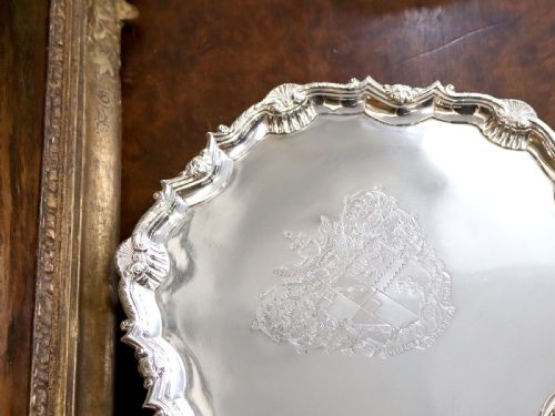 fig 1. A circular Georgian sterling silver salver featuring a pie-crust shell and scroll rim, raised on feet with an engraved coat of arms in the centre.