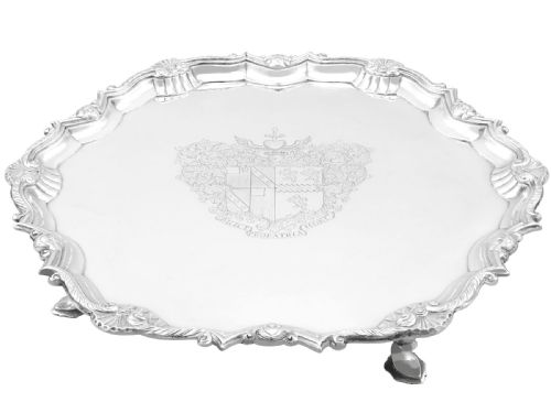 fig 2. A circular Georgian sterling silver salver featuring a pie-crust shell and scroll rim, raised on feet with an engraved coat of arms in the centre.
