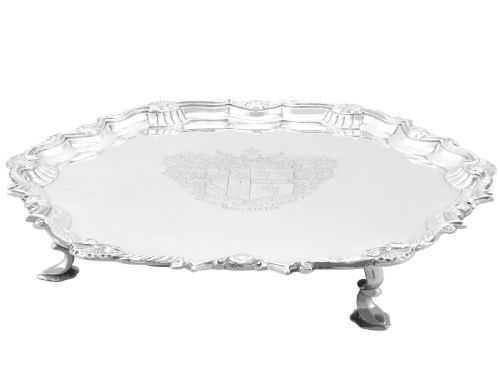 fig 3. A circular Georgian sterling silver salver featuring a pie-crust shell and scroll rim, raised on feet with an engraved coat of arms in the centre.