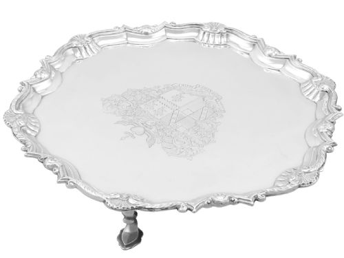 fig 4. A circular Georgian sterling silver salver featuring a pie-crust shell and scroll rim, raised on feet with an engraved coat of arms in the centre.