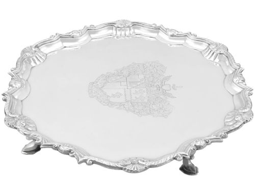 fig 5. A circular Georgian sterling silver salver featuring a pie-crust shell and scroll rim, raised on feet with an engraved coat of arms in the centre.