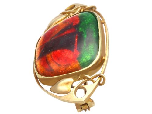 fig 7. An Arts and Crafts 15ct yellow gold brooch featuring a central enamel panel depicting a sailboat against a sunset sky framed by stylized gold leaves.