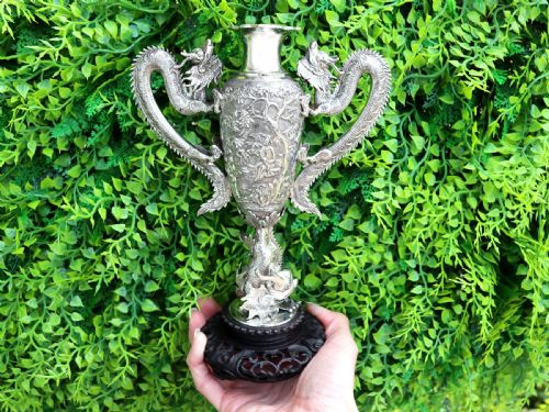 fig 2. A silver trophy-style vase featuring sculpted dragon handles, relief carving, and a dark wooden base.