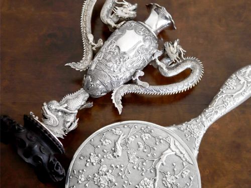 fig 3. A silver trophy-style vase featuring sculpted dragon handles, relief carving, and a dark wooden base.