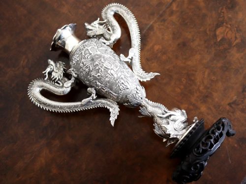 fig 4. A silver trophy-style vase featuring sculpted dragon handles, relief carving, and a dark wooden base.