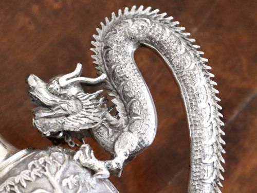 fig 5. A silver trophy-style vase featuring sculpted dragon handles, relief carving, and a dark wooden base.
