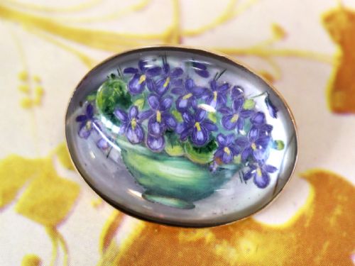 fig 2. An oval 14ct yellow gold brooch set with a reverse-carved glass cabochon displaying purple violets in a green vase.