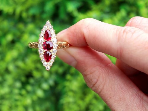 fig 1. An antique 18ct yellow gold navette dress ring featuring three central red rubies surrounded by a border of diamonds and finished with scroll-carved shoulders.
