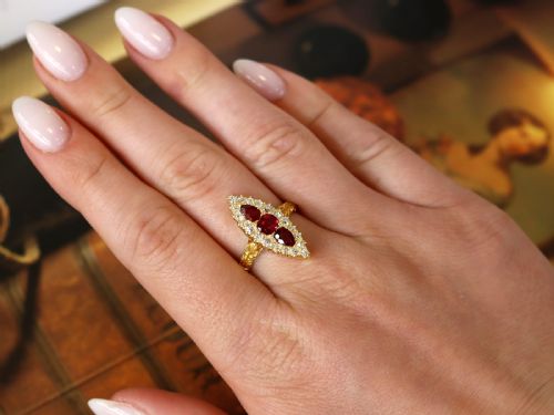fig 2. An antique 18ct yellow gold navette dress ring featuring three central red rubies surrounded by a border of diamonds and finished with scroll-carved shoulders.
