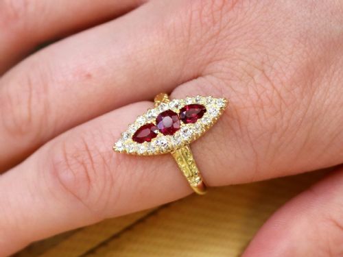 fig 3. An antique 18ct yellow gold navette dress ring featuring three central red rubies surrounded by a border of diamonds and finished with scroll-carved shoulders.