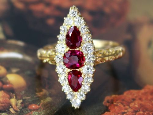 fig 4. An antique 18ct yellow gold navette dress ring featuring three central red rubies surrounded by a border of diamonds and finished with scroll-carved shoulders.