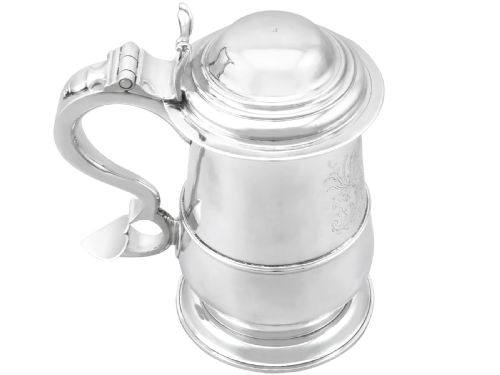 fig 1. A George II sterling silver lidded tankard featuring a domed top, scroll handle, moulded girdle, and engraved foliage decoration.