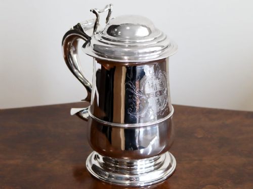 fig 2. A George II sterling silver lidded tankard featuring a domed top, scroll handle, moulded girdle, and engraved foliage decoration.