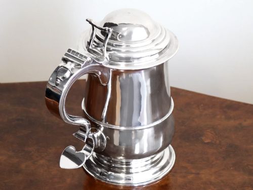fig 3. A George II sterling silver lidded tankard featuring a domed top, scroll handle, moulded girdle, and engraved foliage decoration.