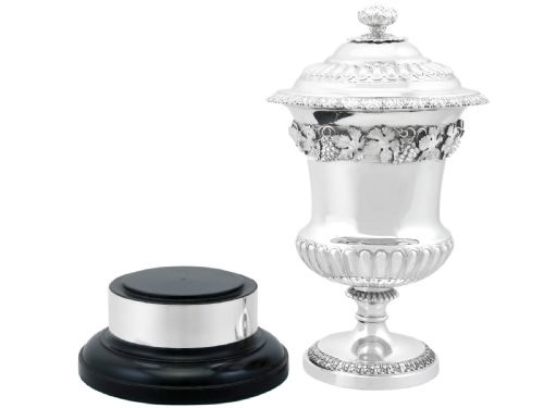 fig 5. A Victorian sterling silver presentation cup and cover decorated with a grape leaf band, resting on a round ebonised wood plinth.
