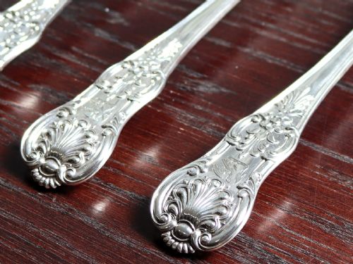 fig 3. Four polished sterling silver gravy spoons displaying intricate Queens pattern scrollwork and shell motifs along their handles, arranged side by side against a white background.