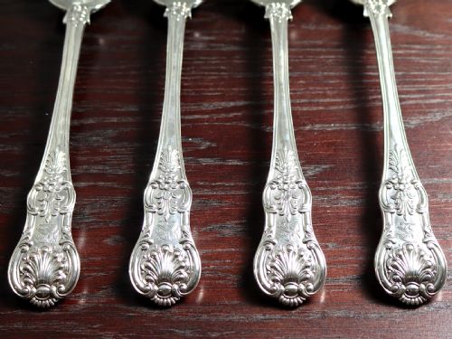 fig 4. Four polished sterling silver gravy spoons displaying intricate Queens pattern scrollwork and shell motifs along their handles, arranged side by side against a white background.