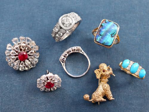 fig 3. A 9ct yellow gold brooch sculpted as a seated poodle with textured fur and red garnet eyes holding a stick in its mouth.