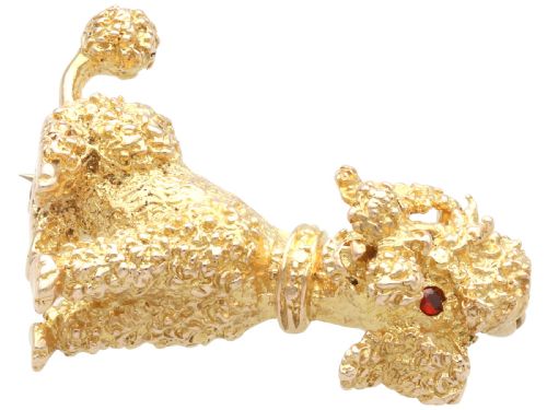 fig 4. A 9ct yellow gold brooch sculpted as a seated poodle with textured fur and red garnet eyes holding a stick in its mouth.